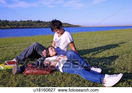 Stock Photo - Young couple sitting and lying on the lawn with smile,. Fotosearch