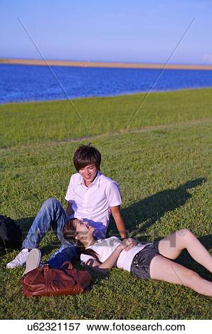 Stock Photo - Young couple sitting and lying on the lawn with smile,. Fotosearch