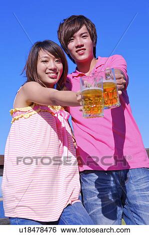Stock Photograph - Young man and woman holding beers and looking at the camera with smile,. Fotosearch