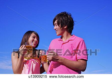 Stock Photography - Young man and woman holding beers and looking at each other with smile,. Fotosearch