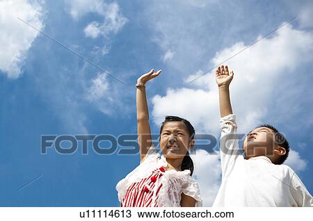 Stock Image - A boy and a girl standing and reaching hands to sky. Fotosearch