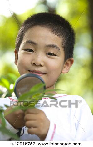 Stock Image - Close-up of boy holding magnifying glass and smiling at the camera. Fotosearch