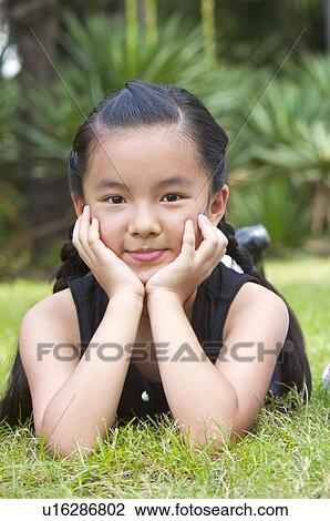 Stock Image - Close-up of girl lying on front with head in hands and smiling at the camera. Fotosearch