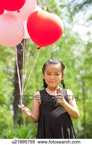 Stock Photo - Girl eating ice cream and holding balloons. Fotosearch