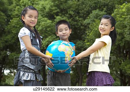 Stock Image - Three children holding the globe together and looking at the camera. Fotosearch