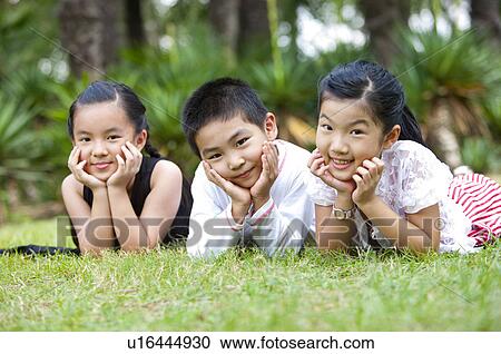 Three children lying on grass with hands on chins, looking at the camera together View Large Photo Image Stock Image - Three children lying on grass with hands on chins, looking at the camera together. Fotosearch
