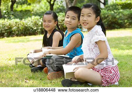 Stock Photo - Three children sitting in a row with book and looking at the camera with smile. Fotosearch