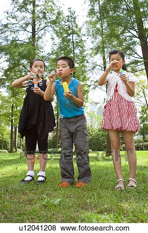 Stock Photo - Three children standing and blowing bubbles together. Fotosearch