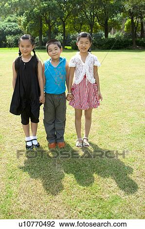Stock Image - Three children standing in a row and holding hands together. Fotosearch