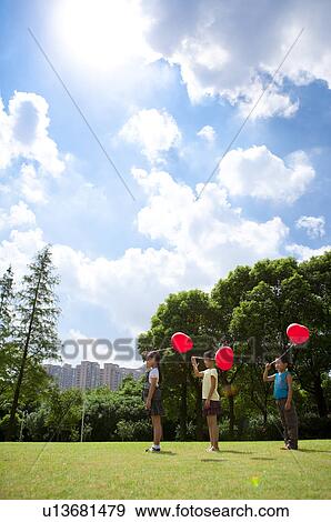 Three children standing in a row and holding balloon together View Large Photo Image Stock Photo - Three children standing in a row and holding balloon together. Fotosearch