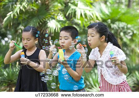 Stock Photo - Three children standing in a row and blowing bubbles together. Fotosearch