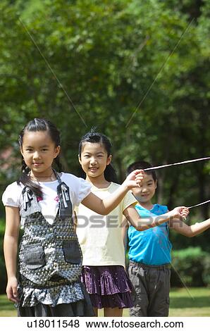 Stock Photo - Three children standing in a row holding a balloon and smiling at the camera. Fotosearch