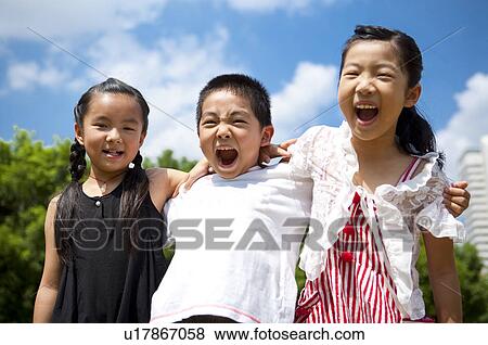 Stock Photo - Three children standing in a row with arms around and shouting happily. Fotosearch