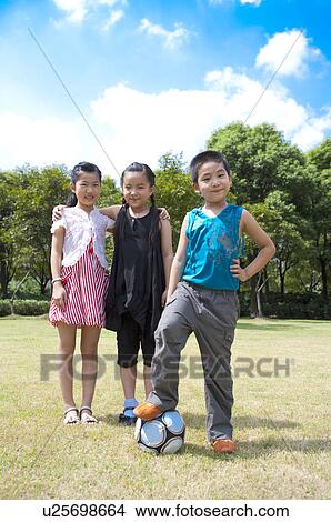 Picture - Three children standing on the lawn with a football and looking at the camera. Fotosearch