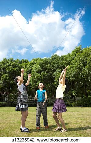 Stock Image - Three children standing on the lawn with arms outstretched and looking up. Fotosearch