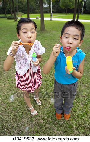 Stock Photo - Two children standing on the lawn and blowing bubbles. Fotosearch