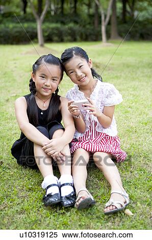 Two girls sitting on the lawn together and looking at the camera with smile View Large Photo Image Stock Photography - Two girls sitting on the lawn together and looking at the camera with smile. Fotosearch