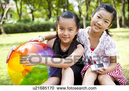 Stock Image - Two girls sitting together with a ball and looking at the camera with smile. Fotosearch