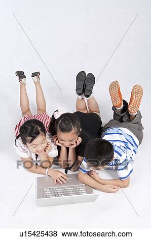 Stock Photo - Child, Children lying on front and using laptop together. Fotosearch