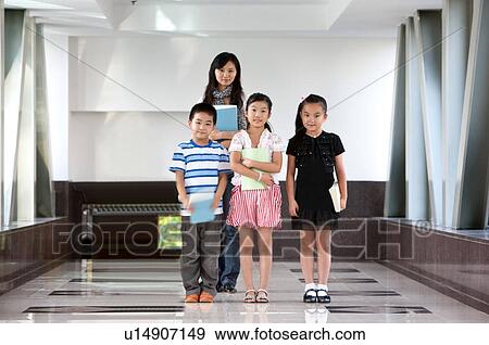 Stock Photo - Child, Children standing in a row with teacher standing behind and holding books. Fotosearch
