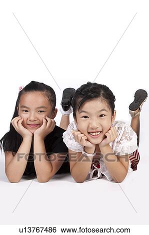 Stock Photograph - Child, Two girls lying on front with head in hands and smiling at the camera. Fotosearch
