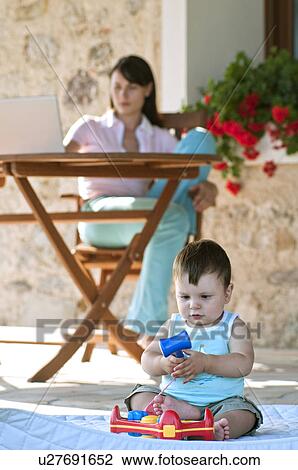 Baby playing with toy and young woman at laptop computer View Large Photo Image Stock Image - Baby playing with toy and young woman at laptop computer. Fotosearch