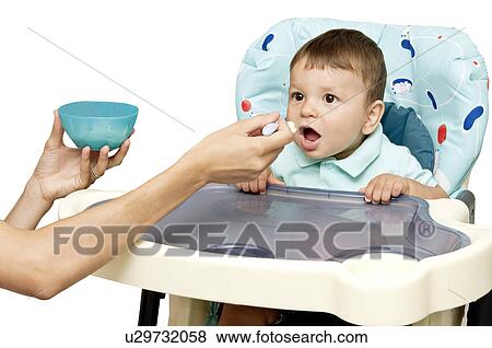 Stock Photo - Young woman's hands feeding baby boy in high chair. Fotosearch