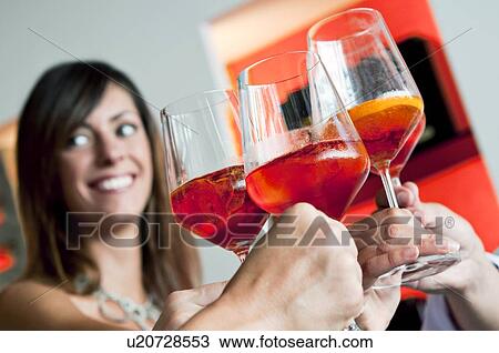 Stock Image - Closeup of young woman's face and other people's hands holding wine glasses and toasting. Fotosearch