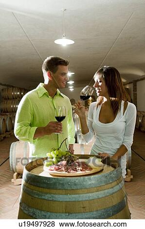 Stock Photo - Couple in a wine cellar tasting red wine and antipasti. Fotosearch