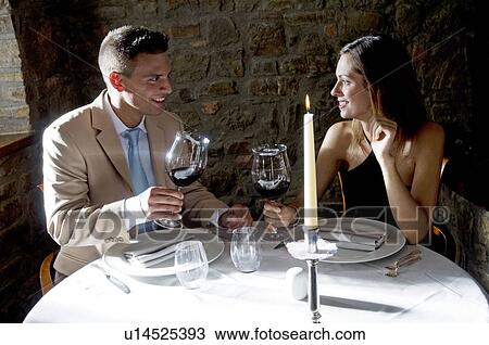 Couple sitting at restaurant table toasting with red wine View Large Photo Image Stock Image - Couple sitting at restaurant table toasting with red wine. Fotosearch