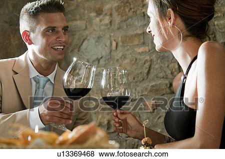 Couple sitting at restaurant table toasting with red wine View Large Photo Image Stock Photo - Couple sitting at restaurant table toasting with red wine. Fotosearch