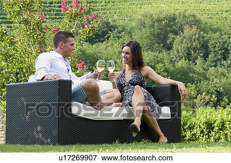 Stock Photo - Young couple sitting on couch in vineyard with white wine. Fotosearch