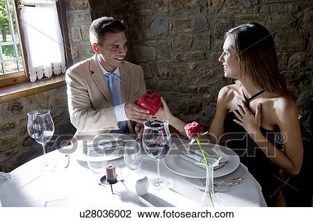 Young man giving a present to young woman at restaurant table View Large Photo Image Stock Image - Young man giving a present to young woman at restaurant table. Fotosearch