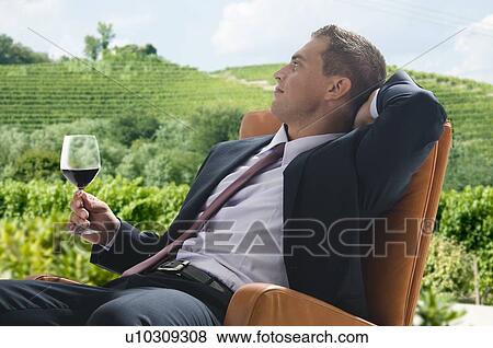 Stock Photo - Young man in business suit sitting with glass of red wine. Fotosearch