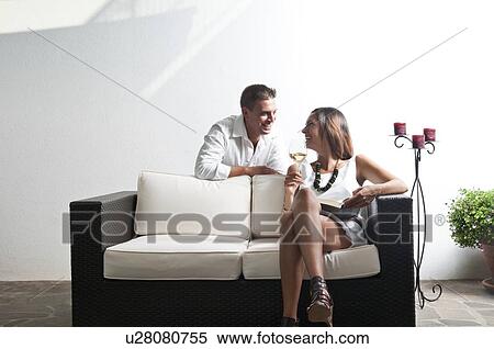 Stock Photography - Young man leaning on couch with young woman with book and white wine. Fotosearch
