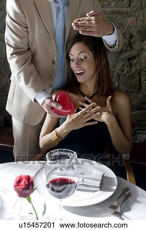 Stock Image - Young man surprising young woman with a present. Fotosearch