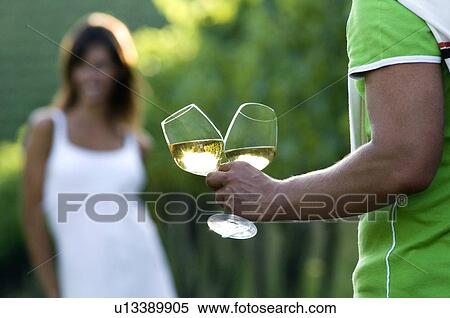 Stock Photography - Young woman in vineyard, man bringing glasses of white wine. Fotosearch