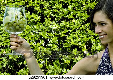 Stock Image - Young woman in vineyard with a wineglass of white grapes. Fotosearch