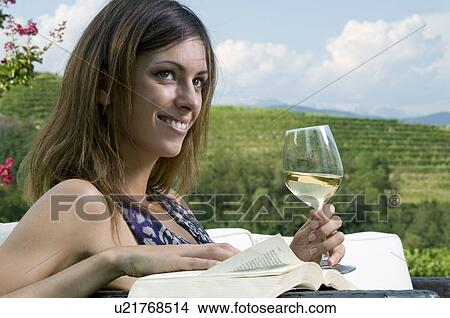 Picture - Young woman sitting in vineyard with white wine and a book. Fotosearch