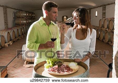 Stock Photo - Couple in a wine cellar tasting red wine and antipasti. Fotosearch