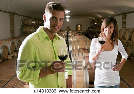Stock Image - Couple in a wine cellar with glasses of red wine. Fotosearch
