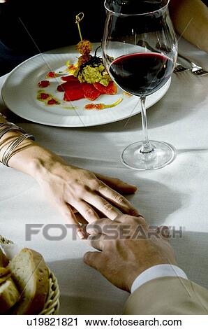 Stock Image - Closeup of couple's hands touching at dinner table. Fotosearch