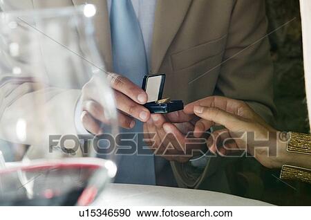Stock Image - Closeup of hands of young man giving a ring to young woman. Fotosearch