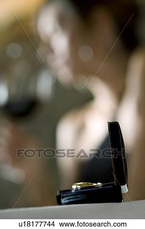 Picture - Closeup of ring with young woman in the background drinking red wine. Fotosearch