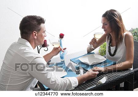 Stock Image - Couple sitting at table drinking white wine. Fotosearch