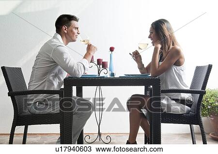 Stock Image - Couple sitting at table drinking white wine. Fotosearch