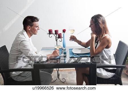 Couple sitting at table drinking white wine View Large Photo Image Stock Photograph - Couple sitting at table drinking white wine. Fotosearch