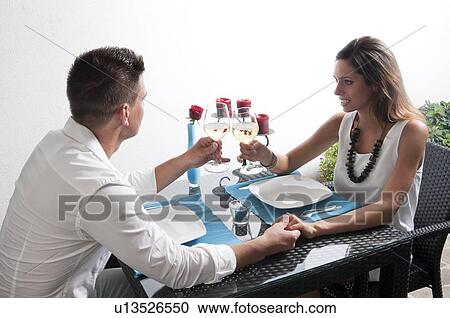 Couple sitting at table toasting with white wine and holding hands View Large Photo Image Stock Image - Couple sitting at table toasting with white wine and holding hands. Fotosearch
