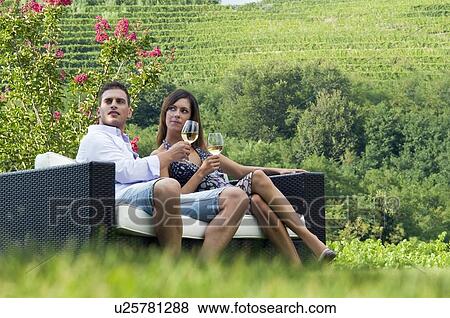 Stock Photo - Young couple sitting on couch in vineyard with white wine. Fotosearch