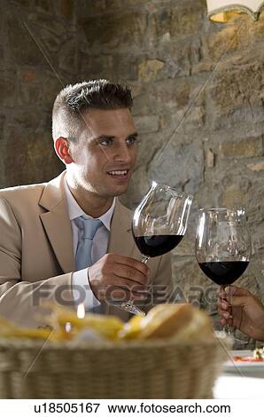 Stock Photo - Young man at restaurant table toasting with wine held by woman's hand. Fotosearch